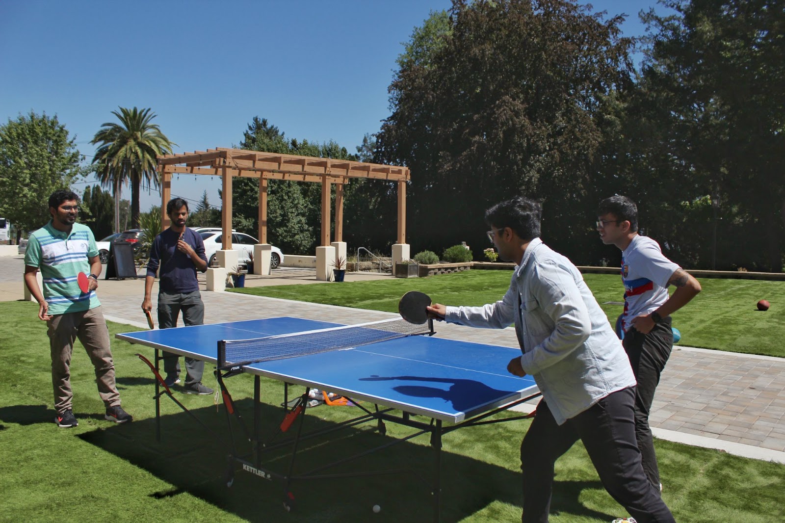 Four residents at the retreat are playing ping-pong or table tennis outdoors. They look very focused.