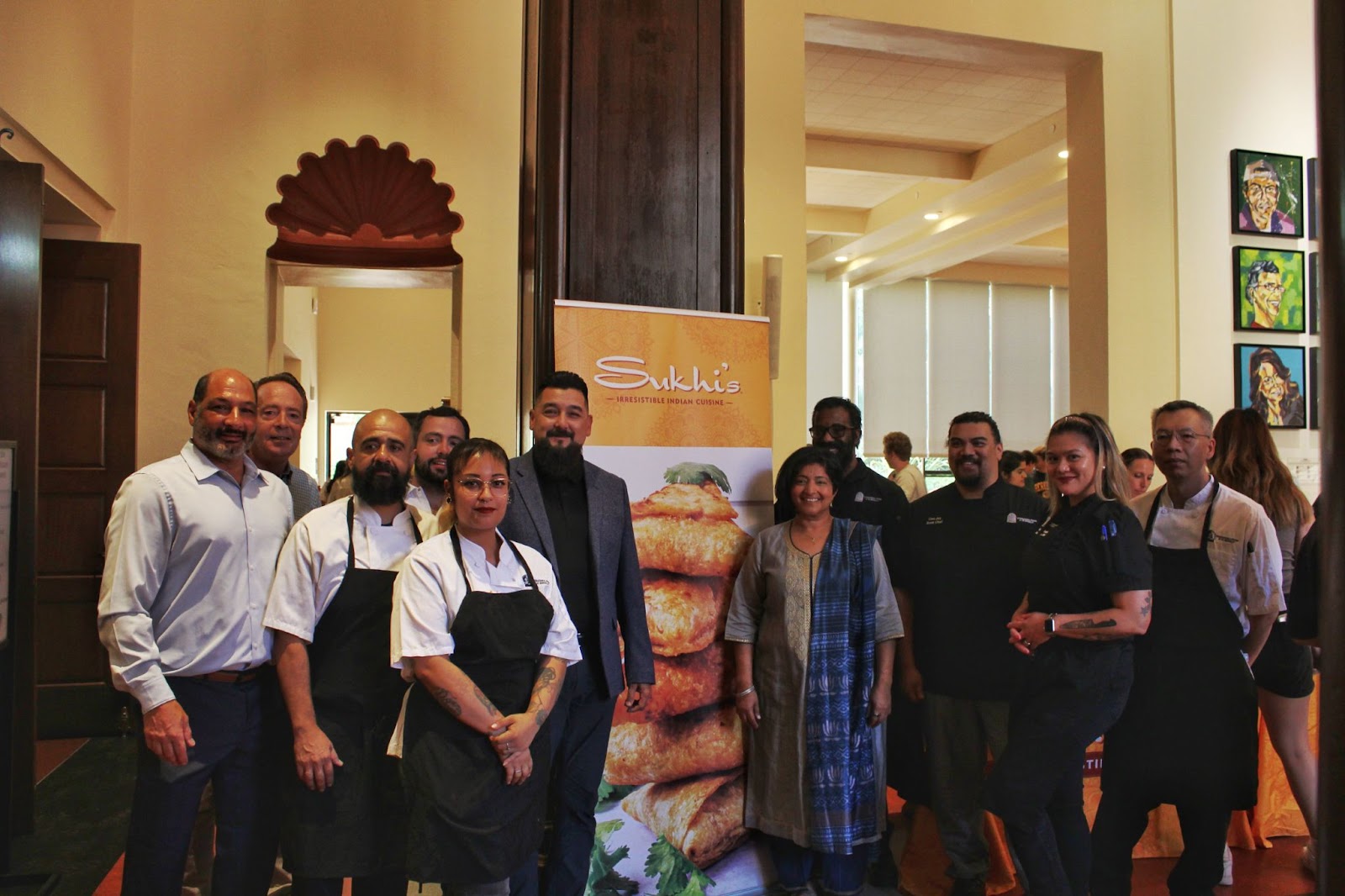 The chef team at International House, Sanjog and Chef Abbie pose for a photograph next to the Sukhi’s banner.