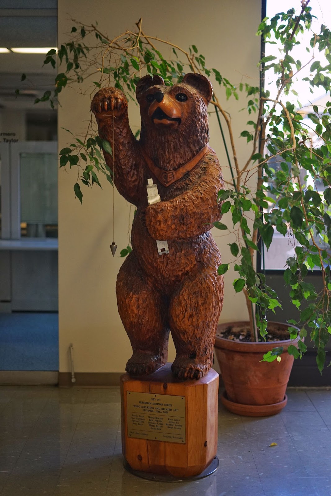 A bear staatue, standing erect, holding a pendulum and a chainsaw.