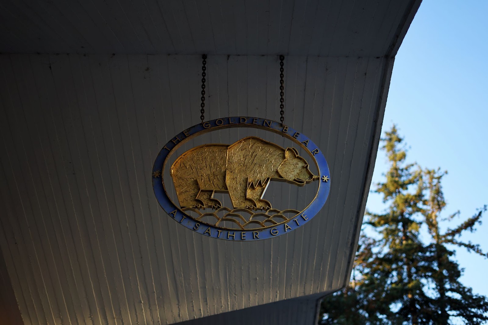 A hanging sign which reads "THE GOLDEN BEAR AT SATHER GATE" and has a bear in the center with golden detailing. 