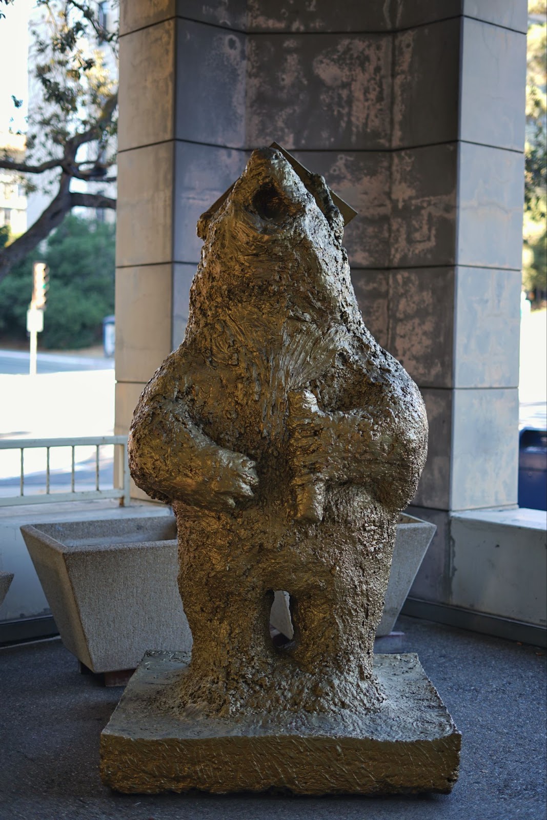 A bear statue, stading erect, seemingly howling, over a platform, while wearing a graduation cap and holding a diploma.