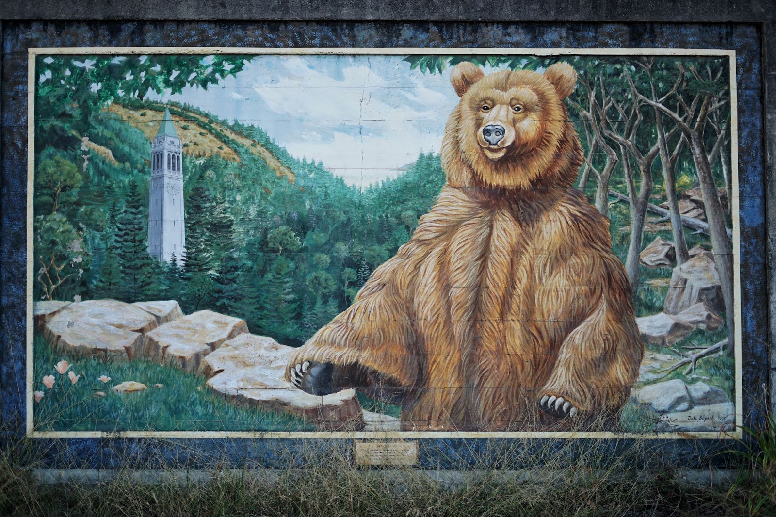 A mural of a bear standing in woods, witht eh Sather Tower in the background.