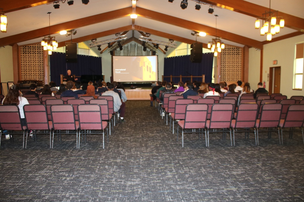 Image of the room showing chairs lines up with an aisle in between and Shawn Carver on the left front of the room presenting.