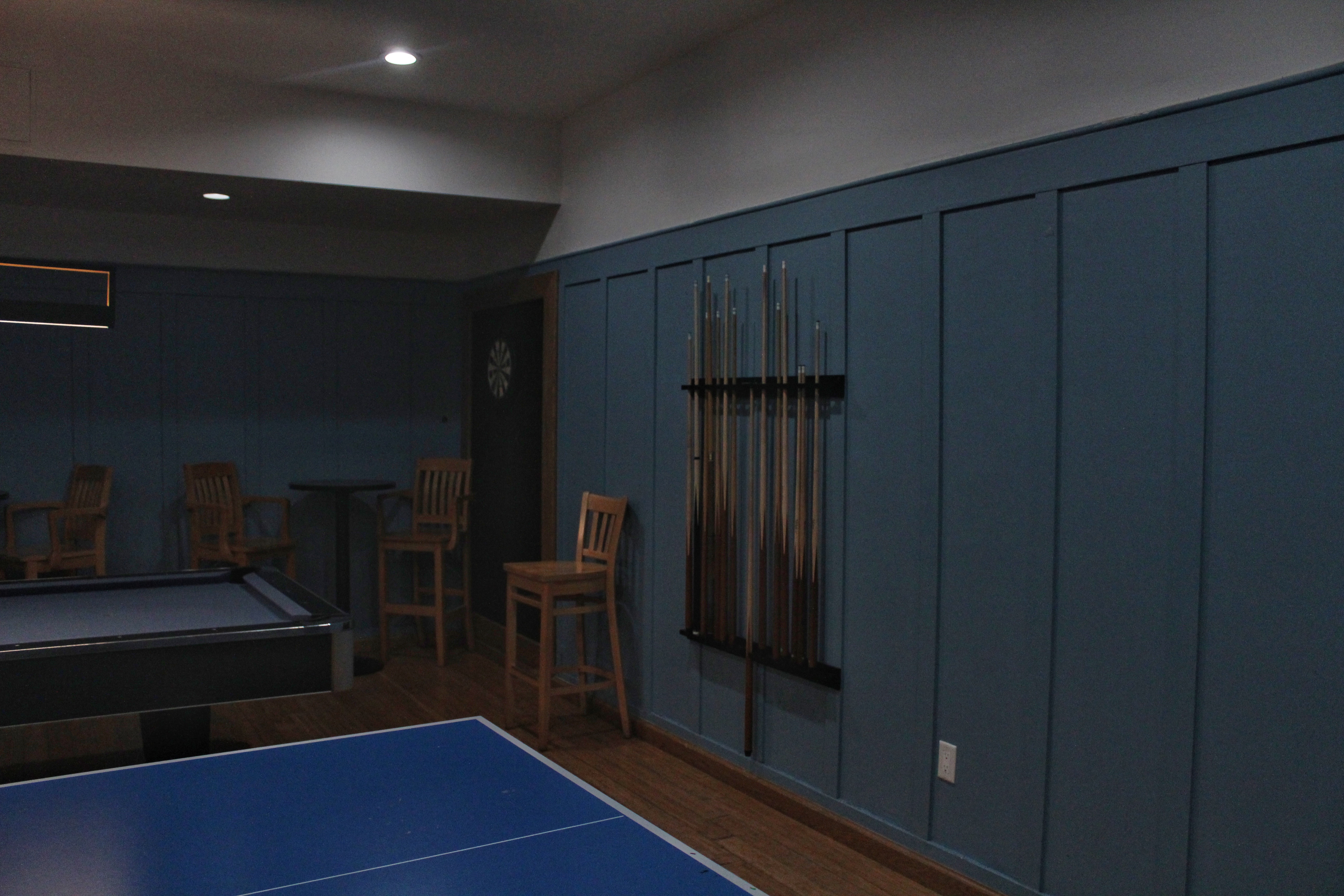 A game room with blue wood-panelled walls and pool equipment.