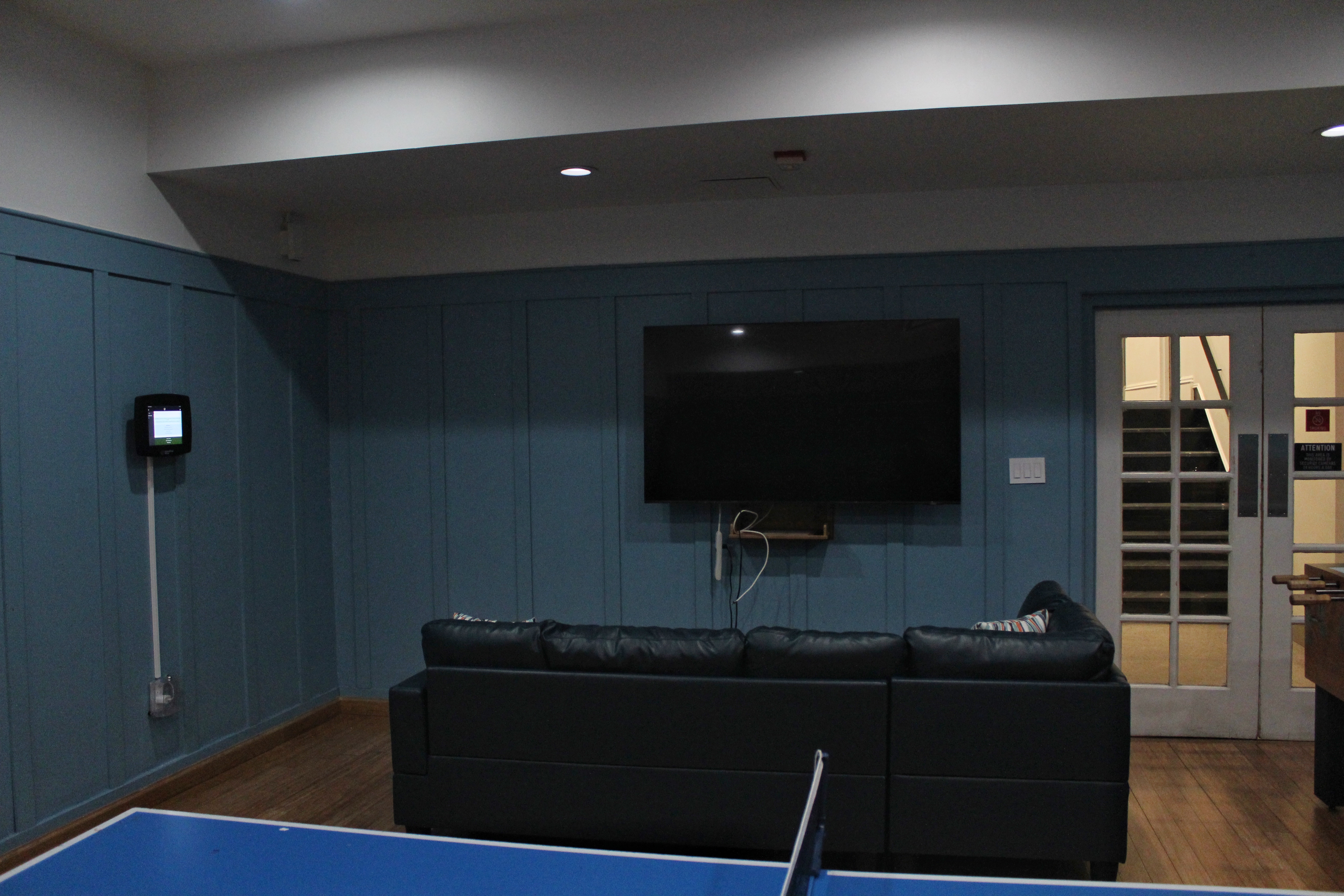 A television with a sofa in front of it on a blue wood-panelled wall.