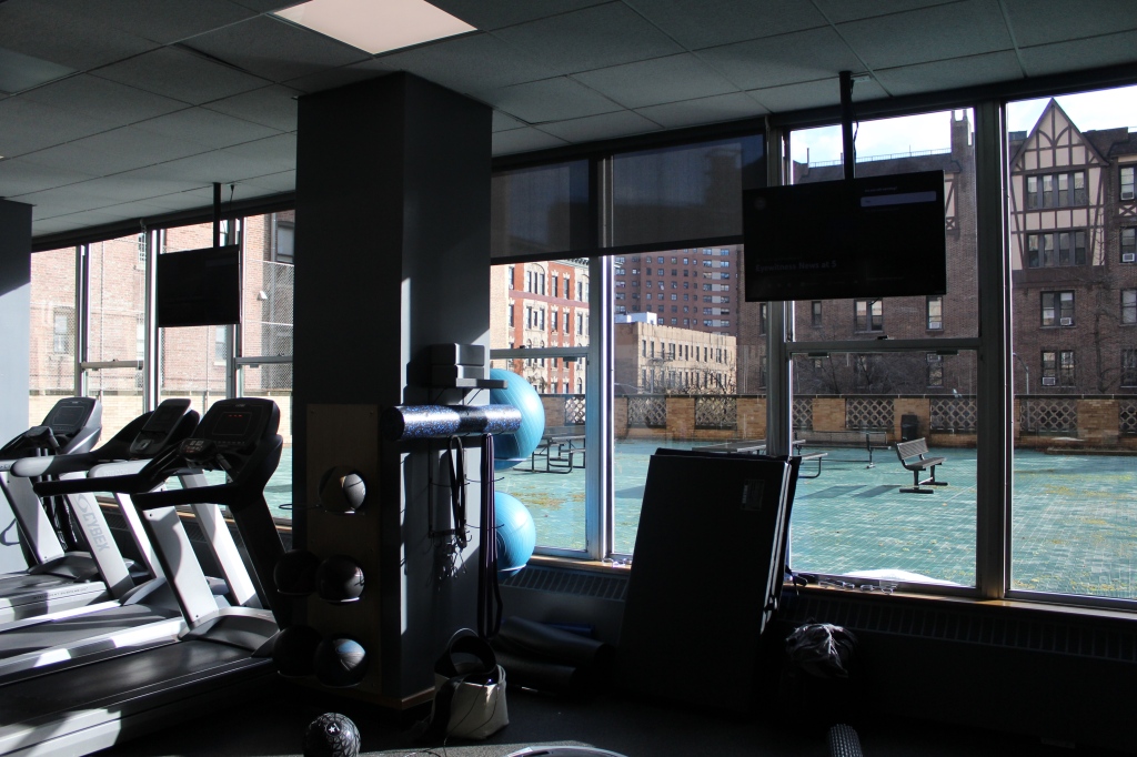 A gym with workout equipment overlooking a rooftop patio.