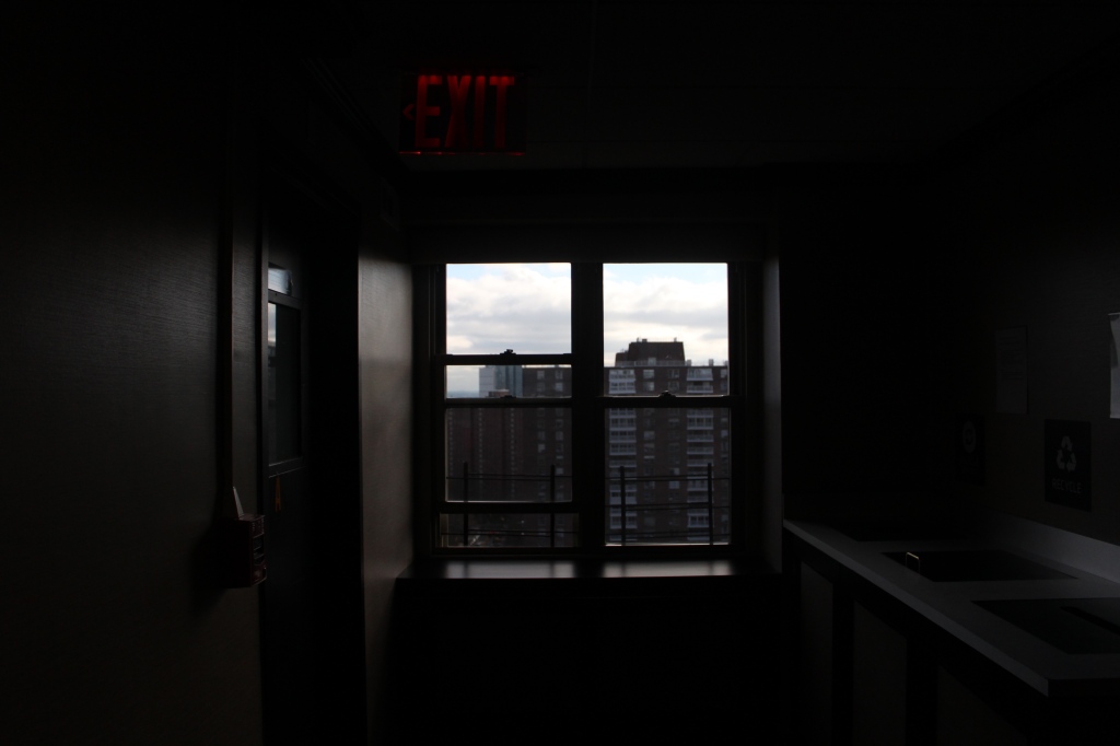 A view of New York buildings through the window of a dimly lit corridor.