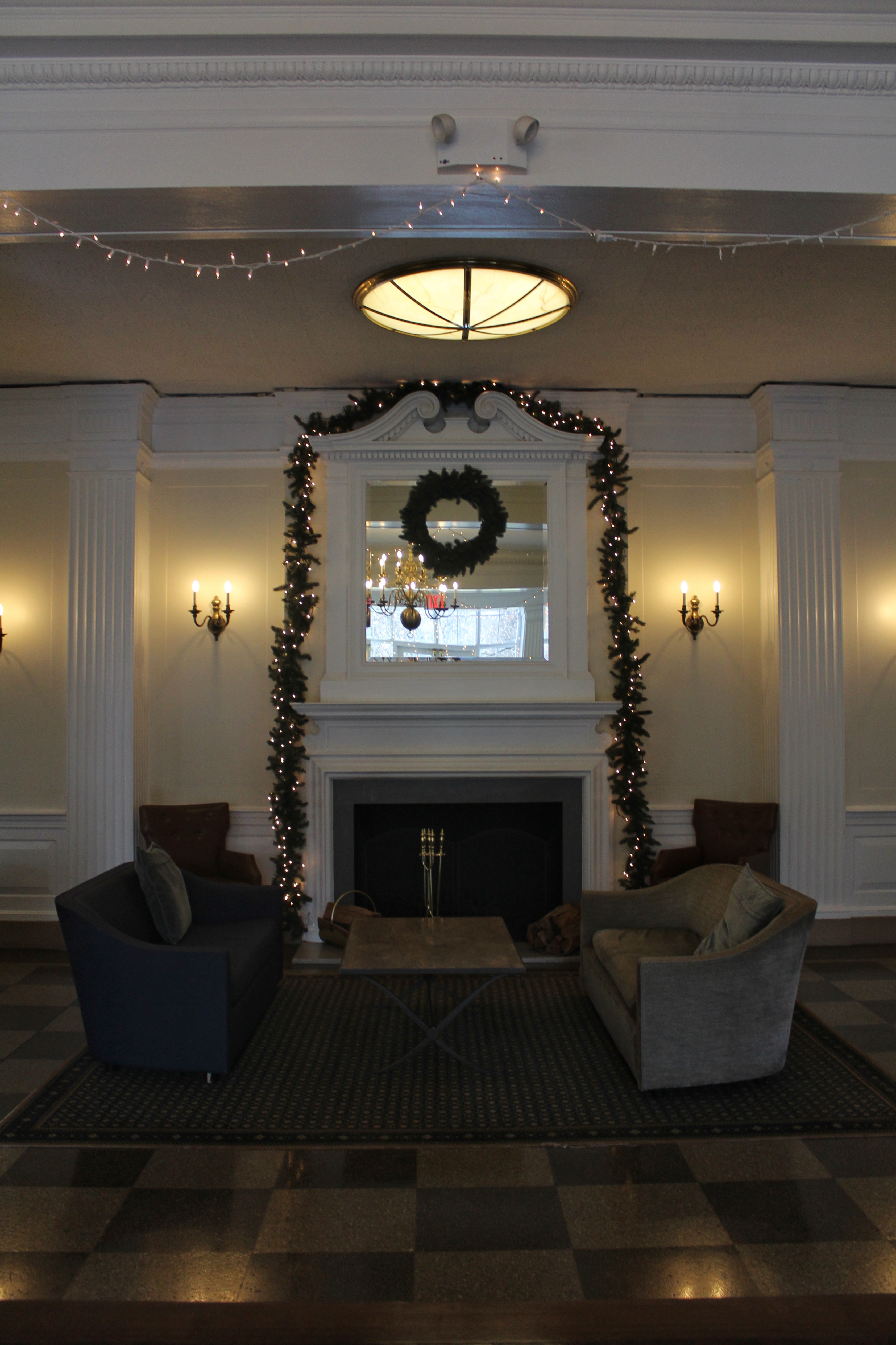 A fireplace with sofas on either side and a wreath adorning the mirror above it. There are Christmas lights on leaves surrounding the mirror.