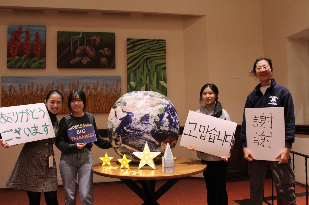 Residents hold up thanks in various languages near a table adorned with a globe and Big Give decorations.