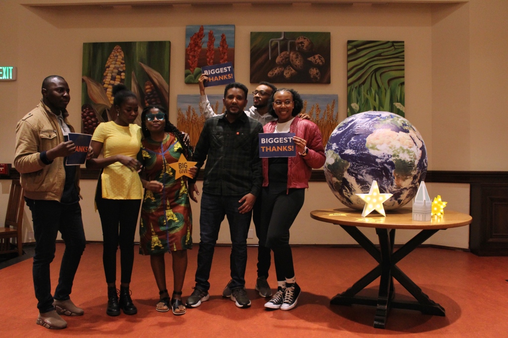 Various residents pose holding Big Give decor near a globe on a table adorned with more Big Give themed decor.
