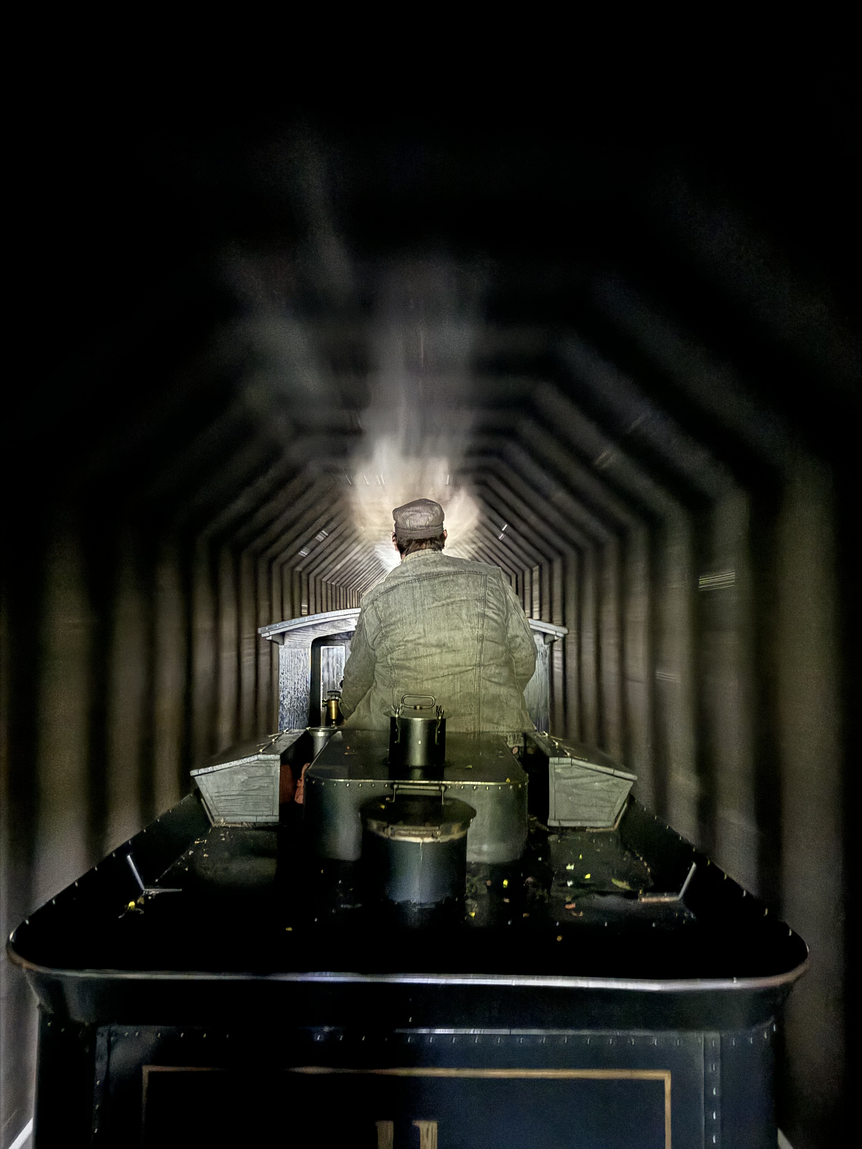 A man operating a miniature steam train through a tunnel.